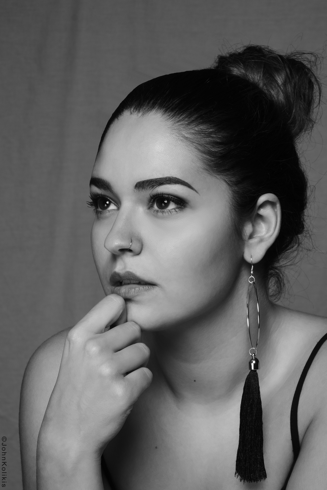 Artistic black and white headshot of a young actress with a thoughtful expression, a nose ring, and a tassel earring.